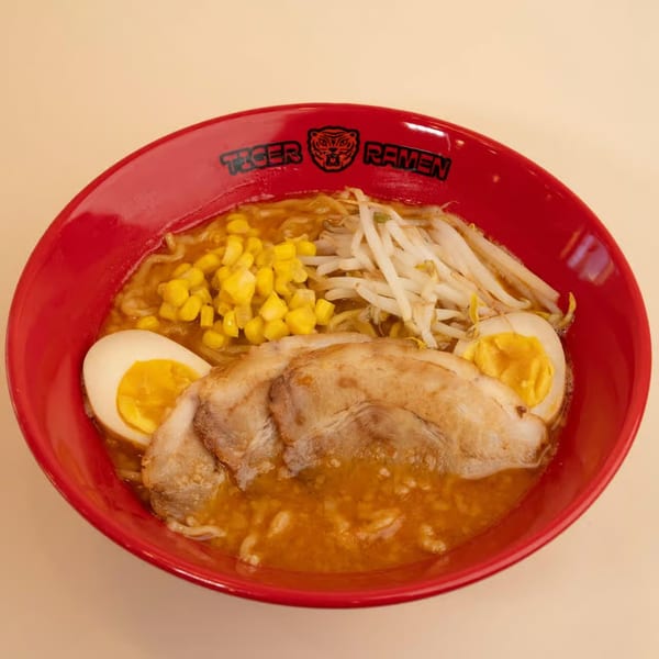 A red bowl of Tiger Ramen with pork, corn, bean sprouts, and two hard-boiled egg halves.