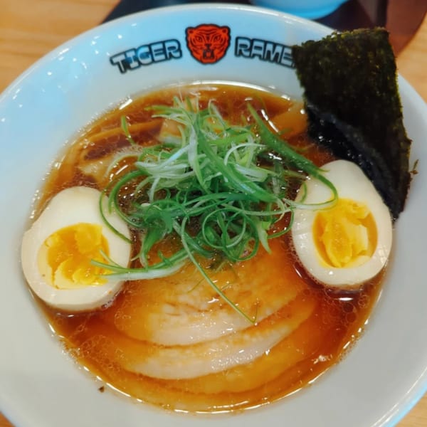 A bowl of Tiger Ramen with broth, pork, green onions, nori, and two soft-boiled eggs.