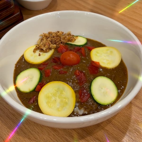 Tiger Ramen's curry dish with zucchini, squash, tomato, and fried onions in a white bowl.